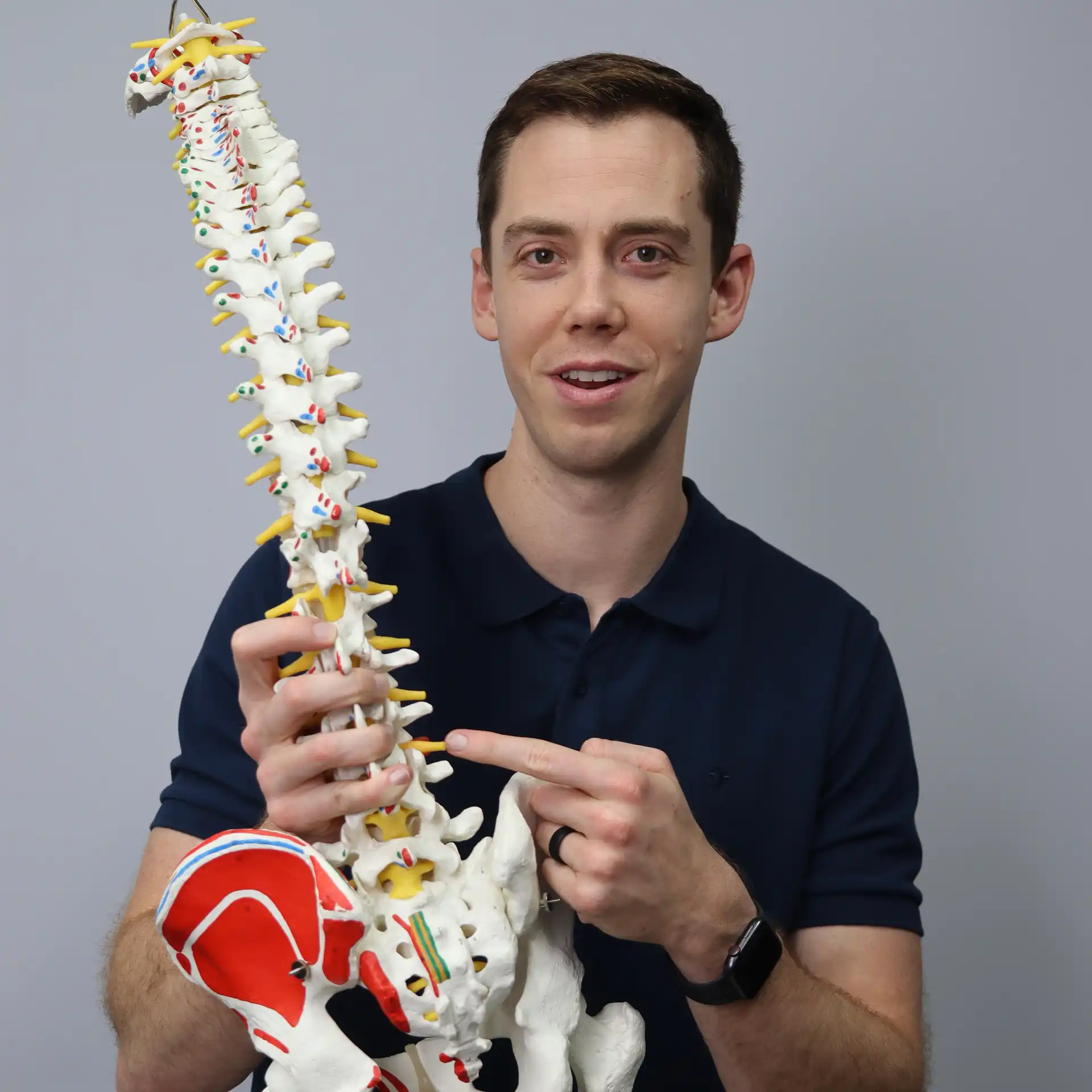 Dr. Brandon Launstein, DPT, holding an anatomical spine model